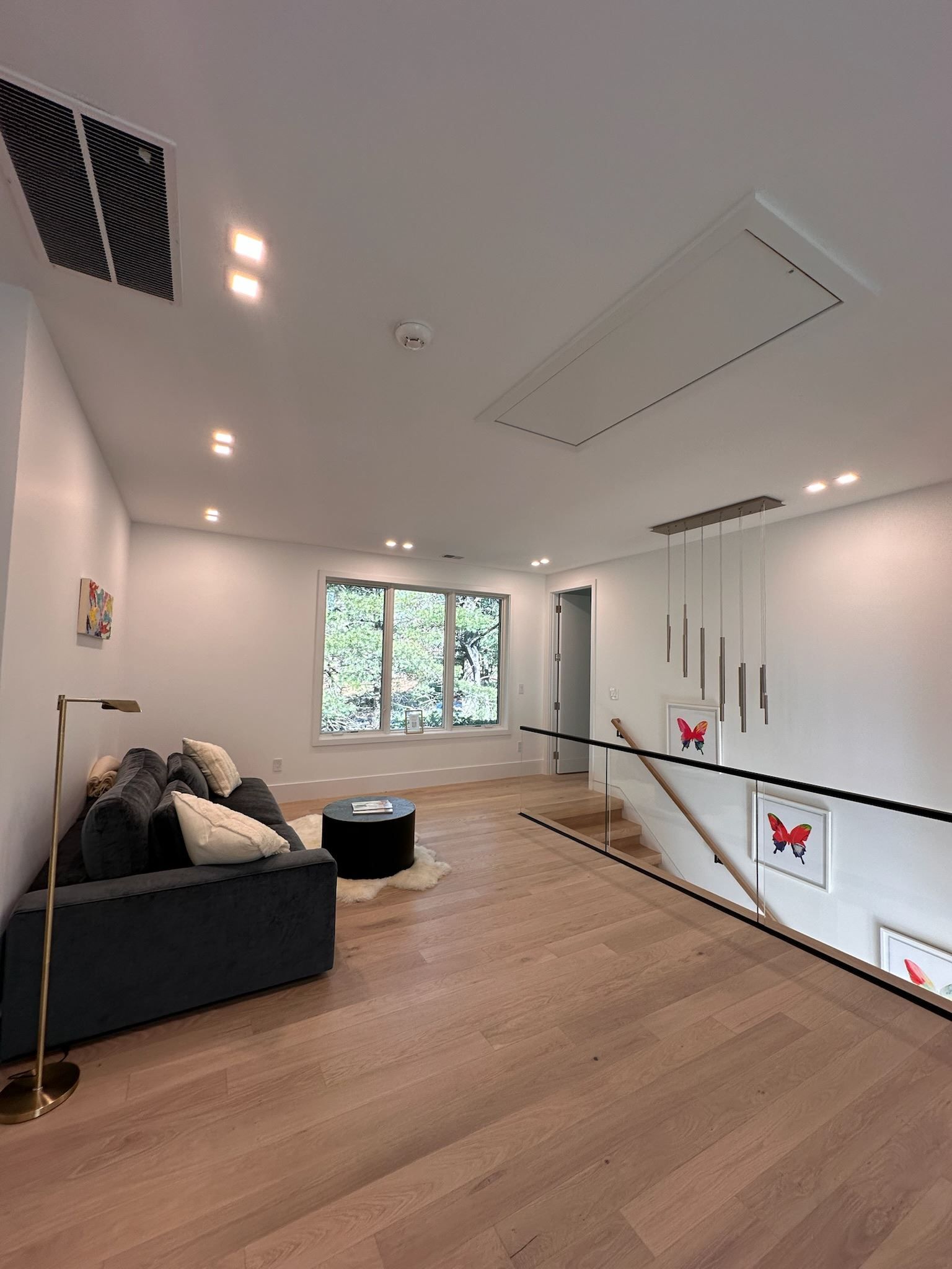 Modern living room with gray sofa, wood floor, white walls, skylight, and large window.