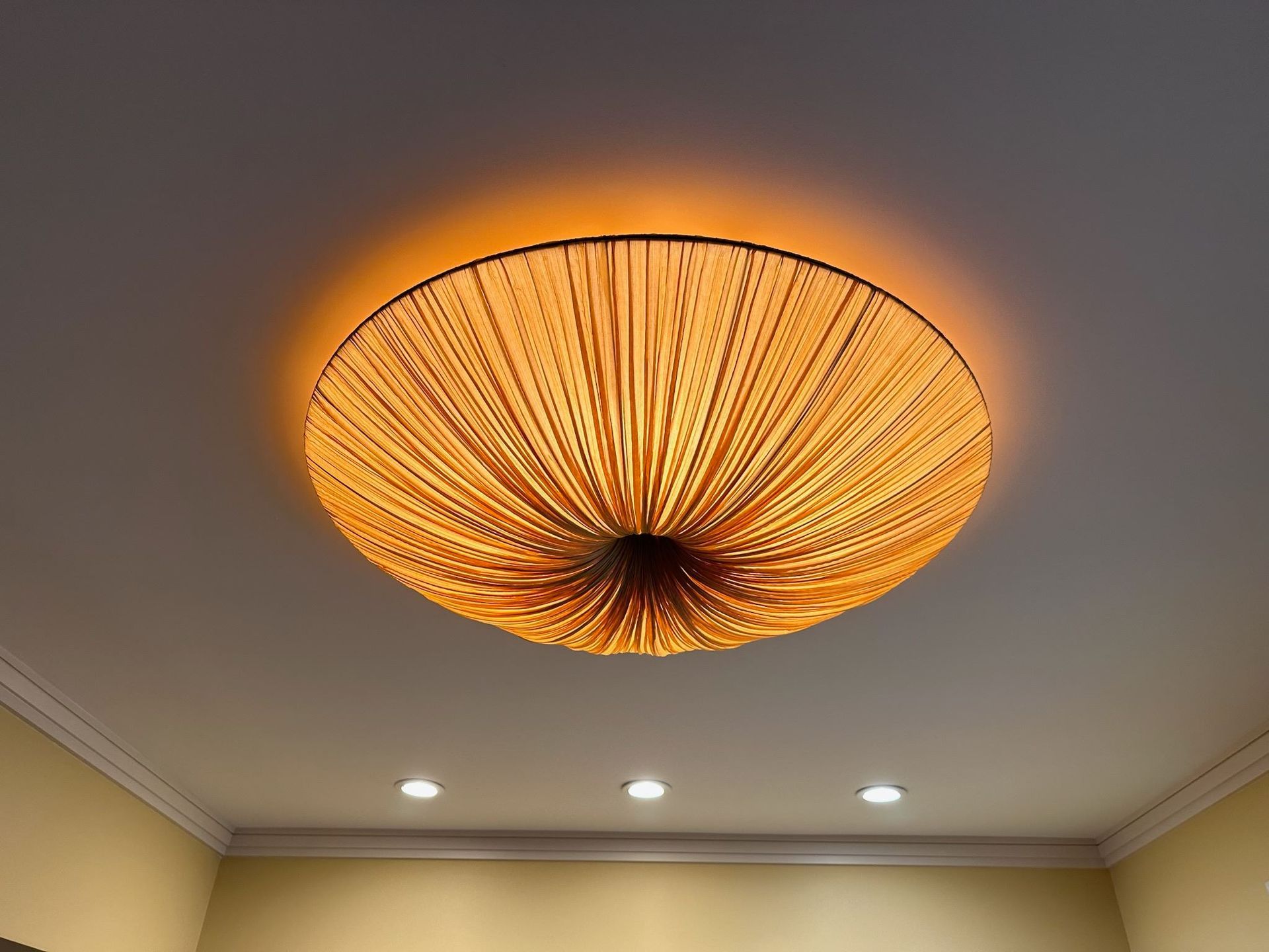 Orange woven ceiling light fixture glowing on a beige ceiling
