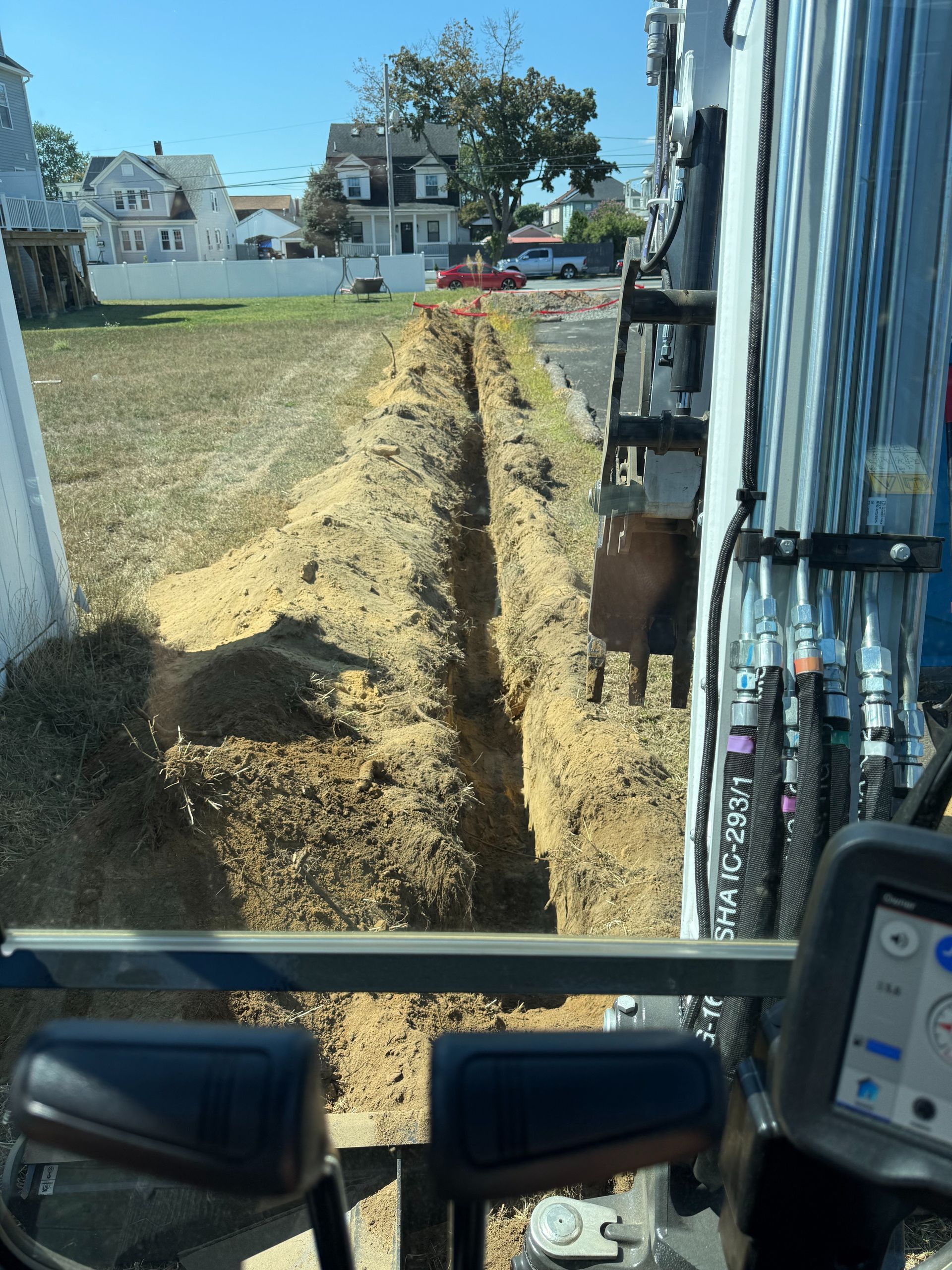 View from an excavator over a dug trench beside a blue building in a grassy yard