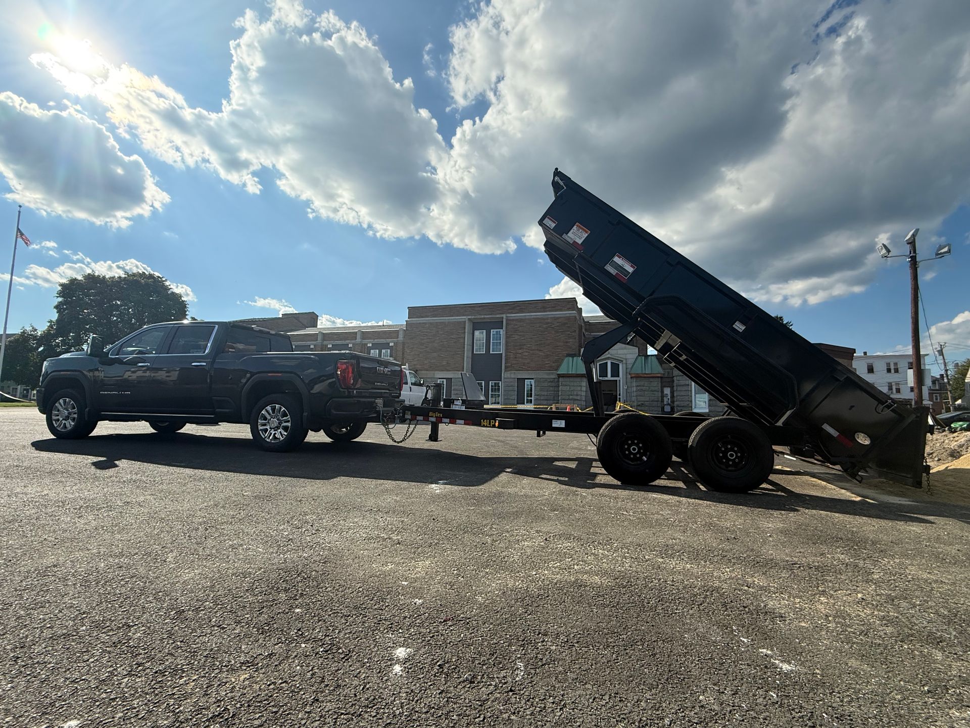 Black dump trailer attached to a truck in a gravel lot under a cloudy sky.