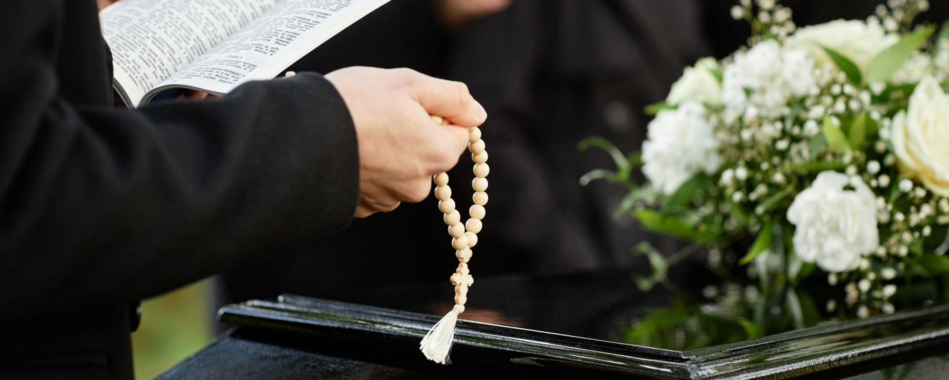 Close up of person in black praying at outdoor funeral and holding Bible with rosary