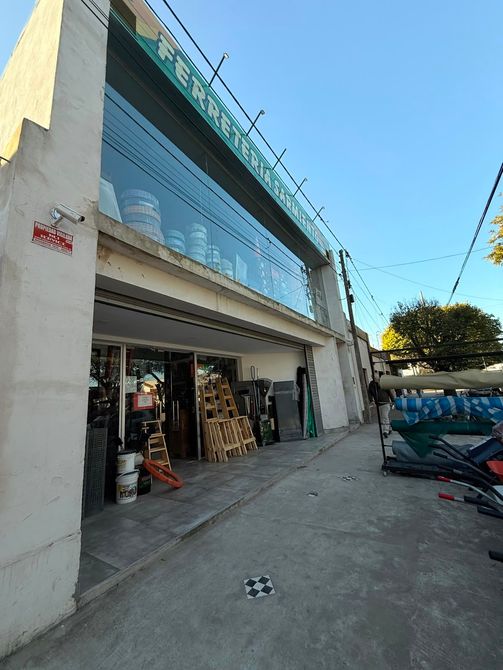 Local comercial moderno con fachada de cristal, entrada abierta y vehículos estacionados a lo largo de una acera soleada.