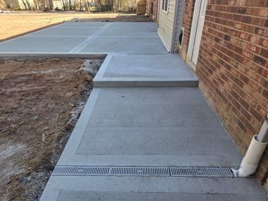 Concrete sidewalk and driveway beside a brick house, with a drain grate and a small step up to the door