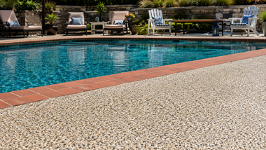 Outdoor swimming pool with blue water, brick edge, and lounge chairs in the background