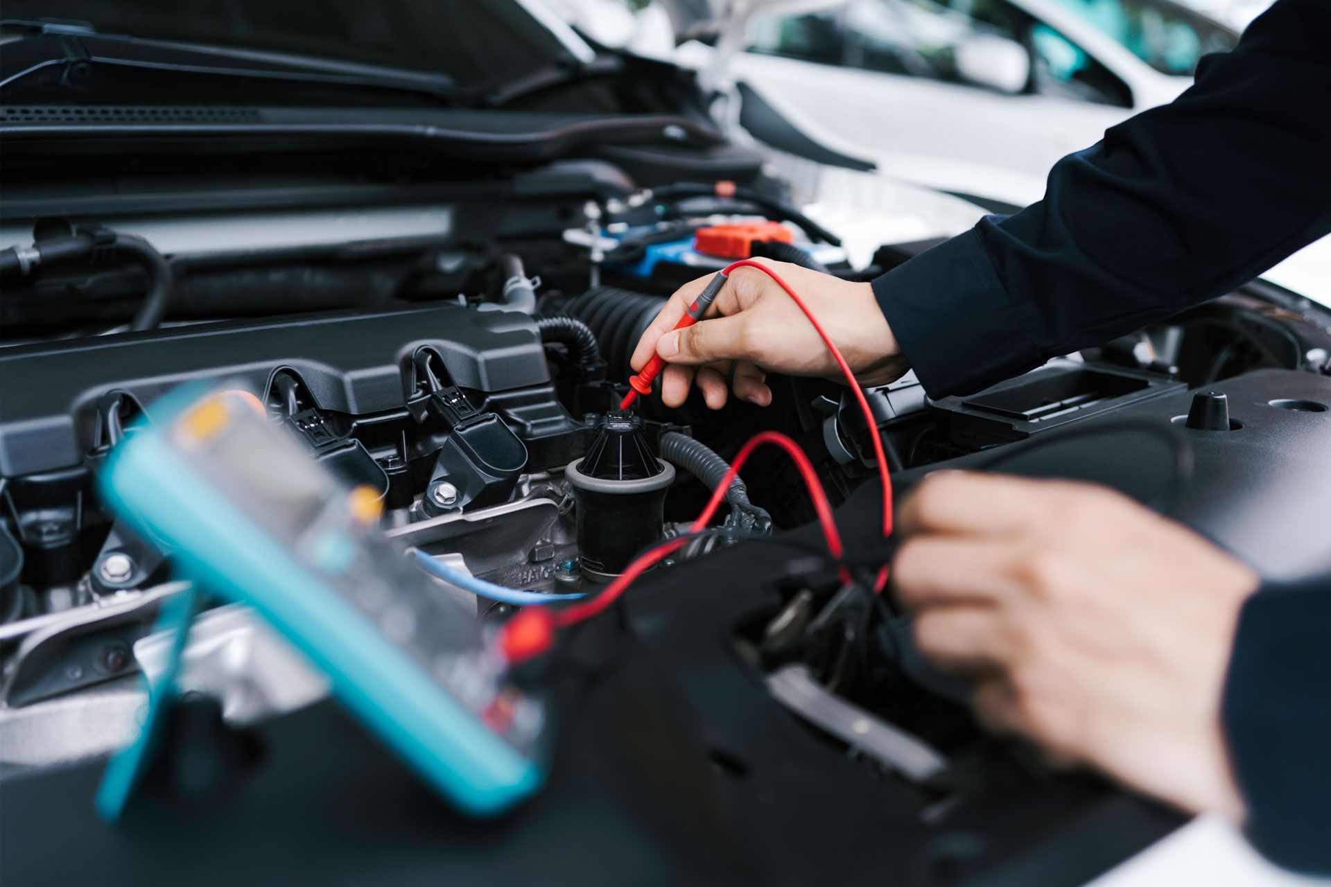 Mechanic using multimeter on a car engine, testing wires.