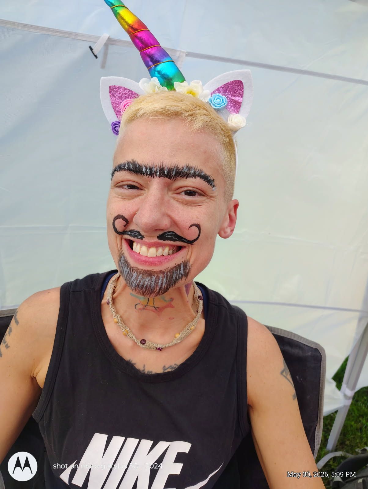 Smiling person in a black Nike tank top wearing a colorful unicorn headband and playful face paint.