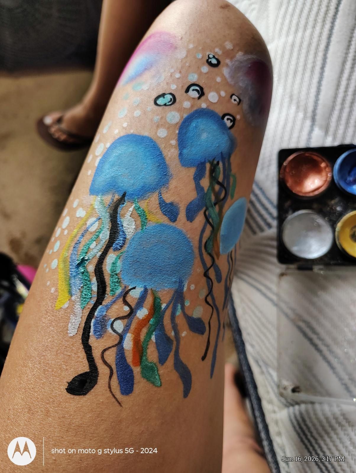 Blue jellyfish body art painted on a leg, with colorful tentacles and a watercolor palette nearby