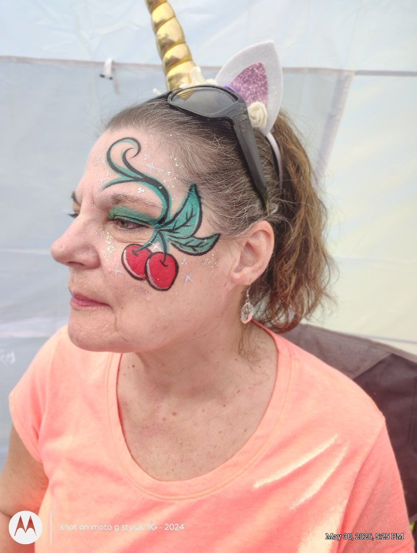 Woman with unicorn face paint, gold horn headband, and coral shirt, shown in side profile against a plain backdrop