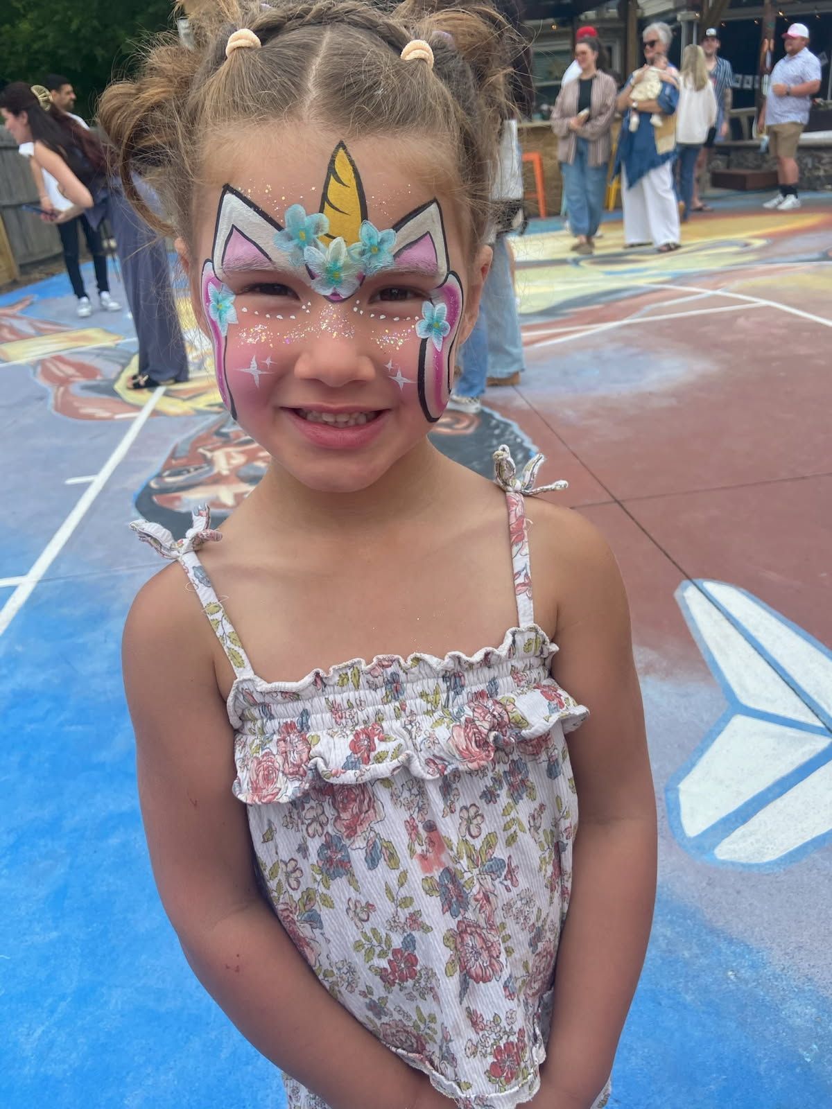 Smiling child with colorful butterfly face paint and braided hair at an outdoor event
