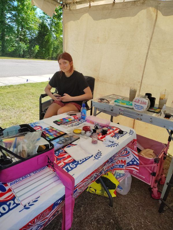 Person seated at a table with colorful snacks and items at an outdoor booth under a tent