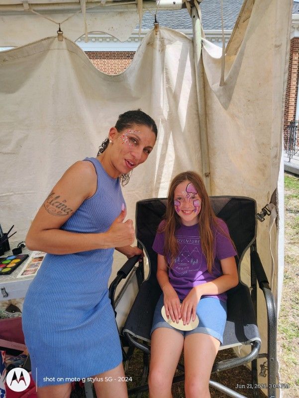 Two people posing under a canopy, one standing and one seated, both smiling and giving thumbs up.