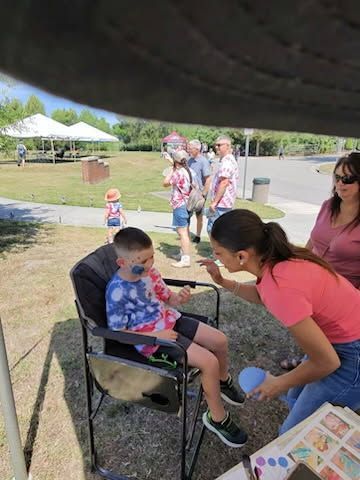 Child in a chair getting face painting under a canopy at an outdoor event