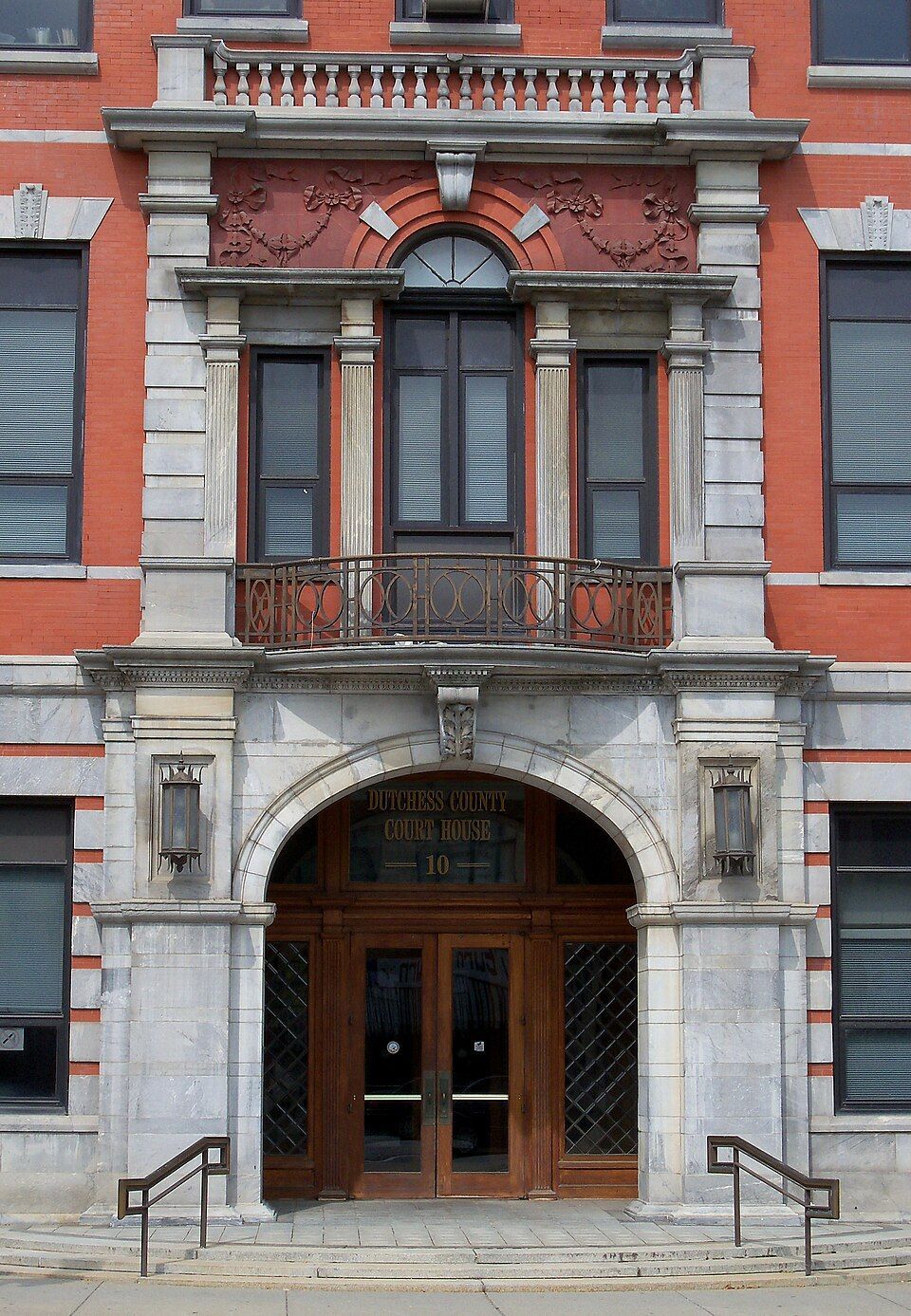 Red-brick historic building facade with arched entrance, wooden double doors, and stone trim