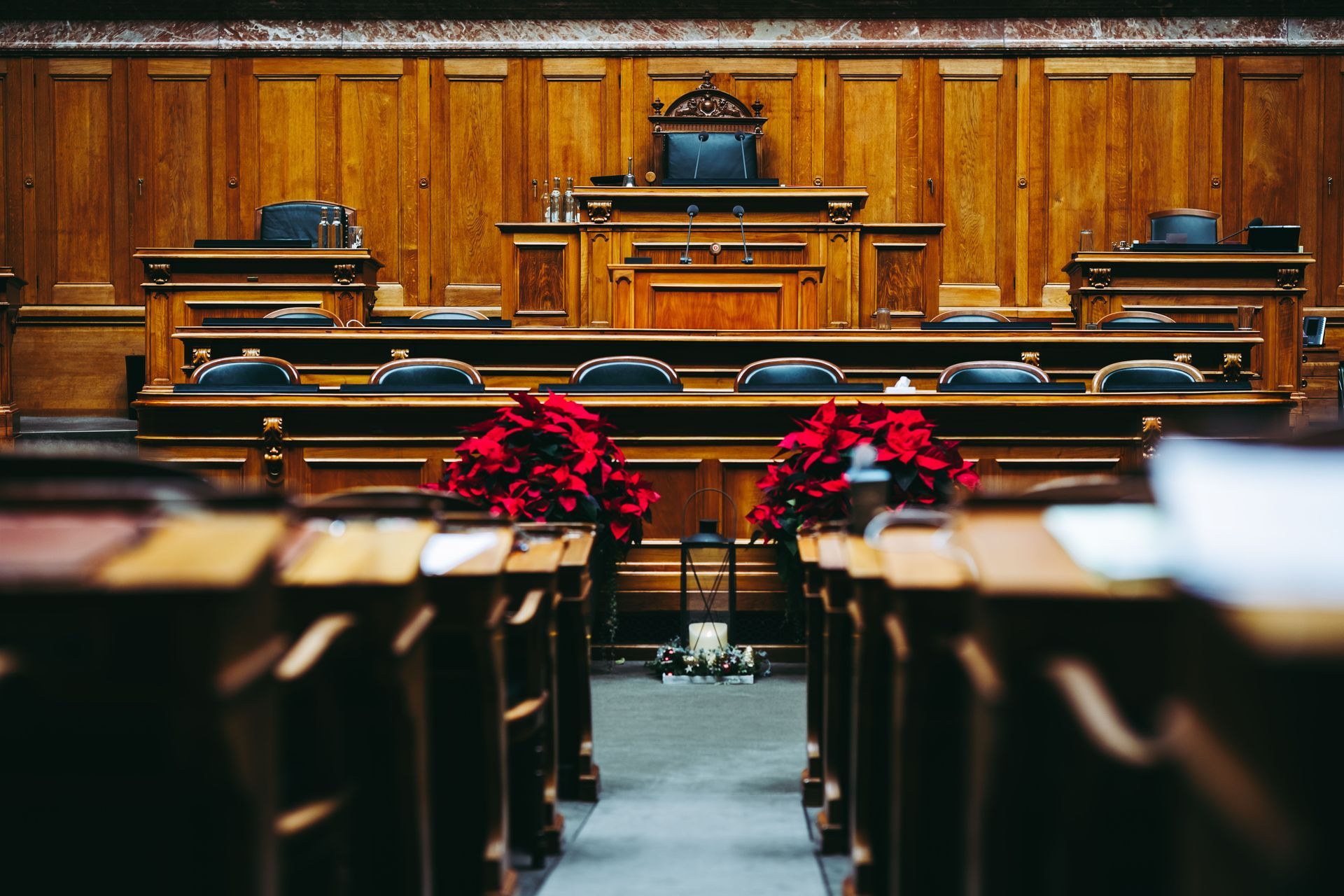 Empty wood-paneled courtroom with benches, judge’s bench, and red poinsettias in the foreground