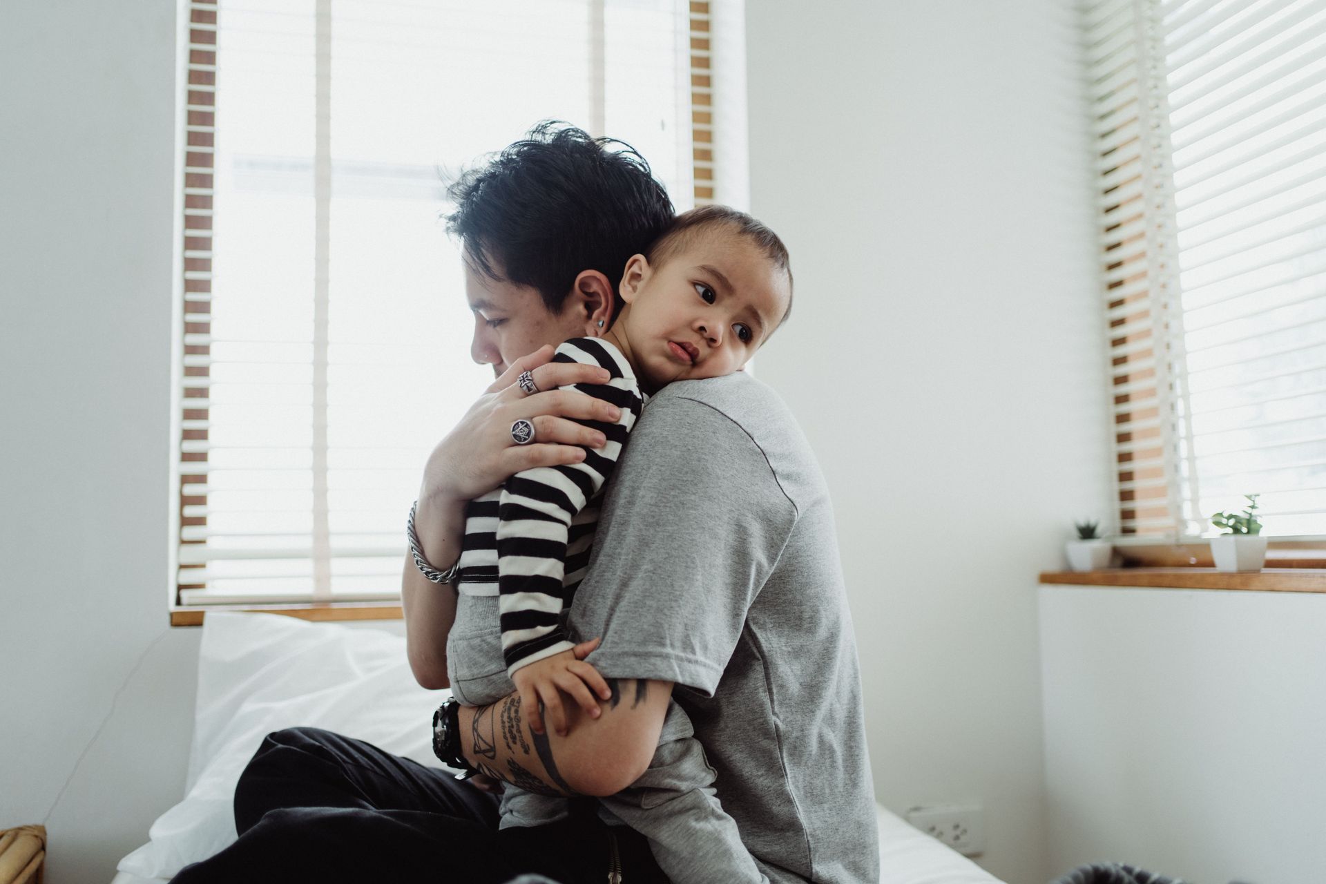 Person hugging a smiling child on a bed in a bright room by a window