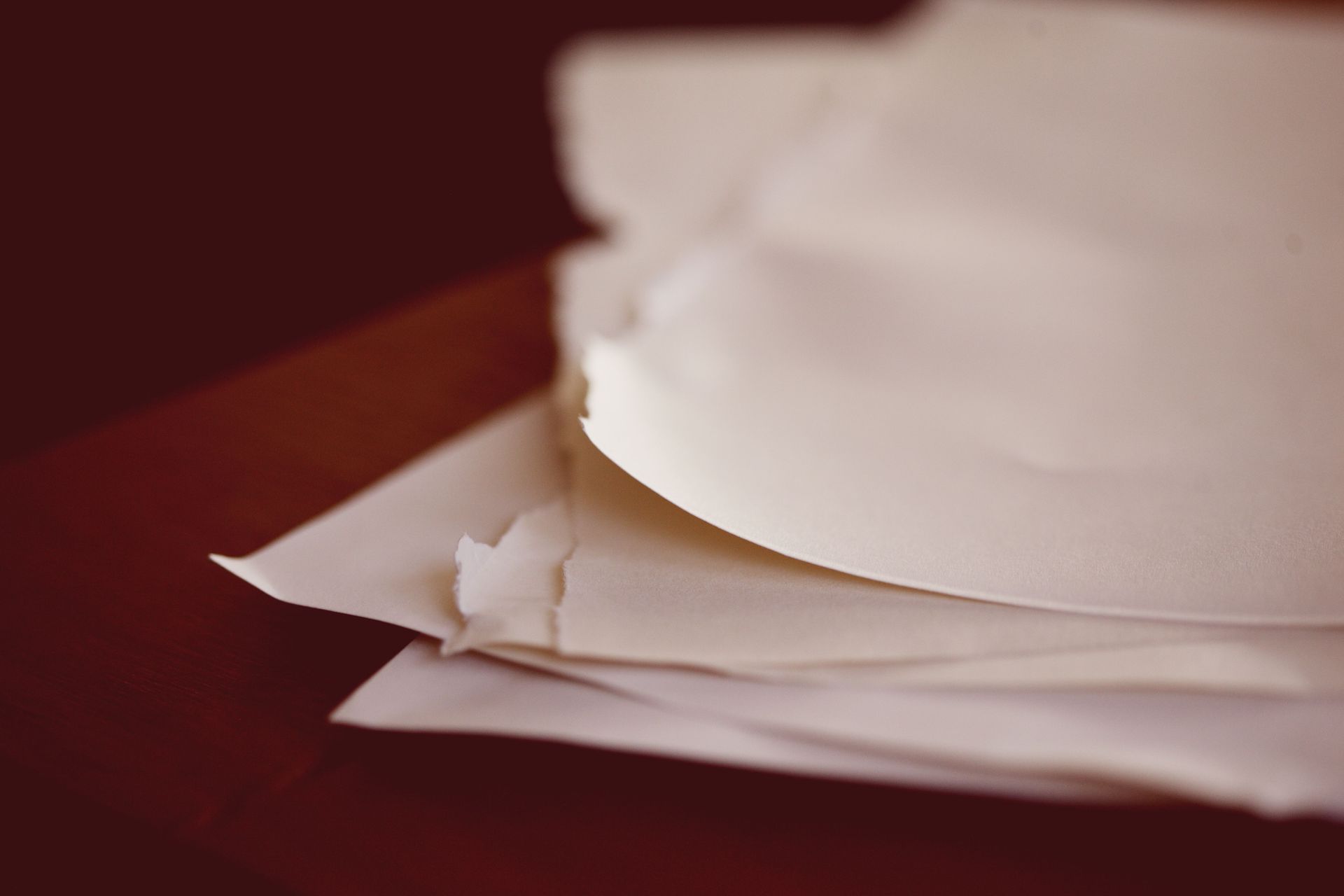 Stack of white paper sheets on a dark red surface, with torn edges in the foreground.