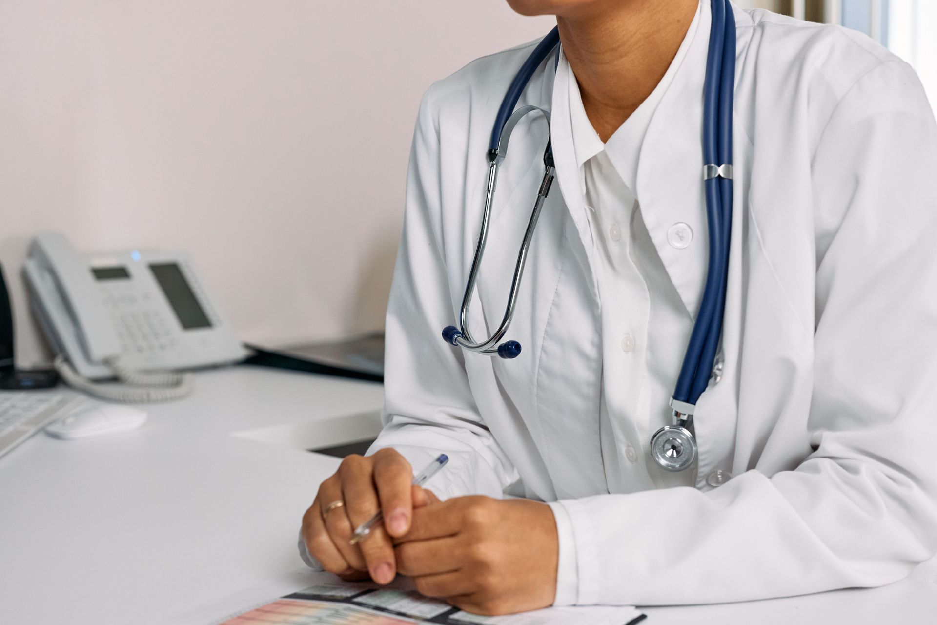 Doctor in a white coat with stethoscope seated at a desk in a clinic office