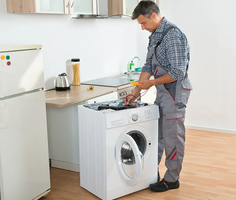 Un hombre está arreglando una lavadora en una cocina.
