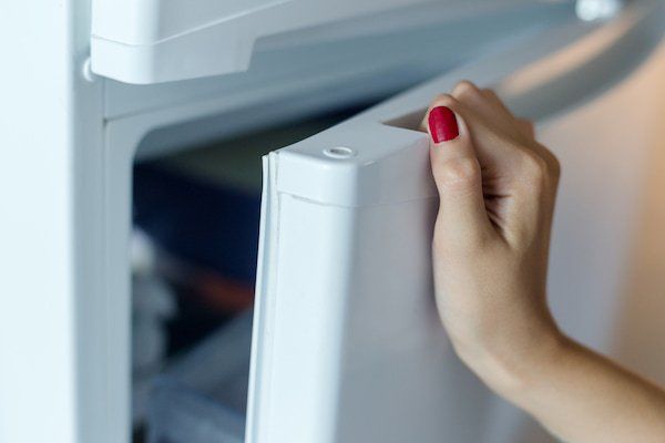 Una mujer con uñas rojas abre la puerta de un refrigerador.