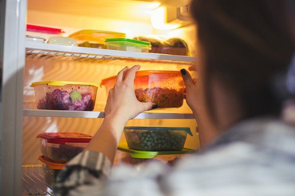 Una mujer saca un recipiente de comida de un frigorífico.
