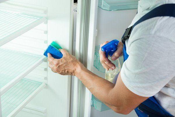 Un hombre está limpiando la puerta de un refrigerador con una esponja y una botella de spray.