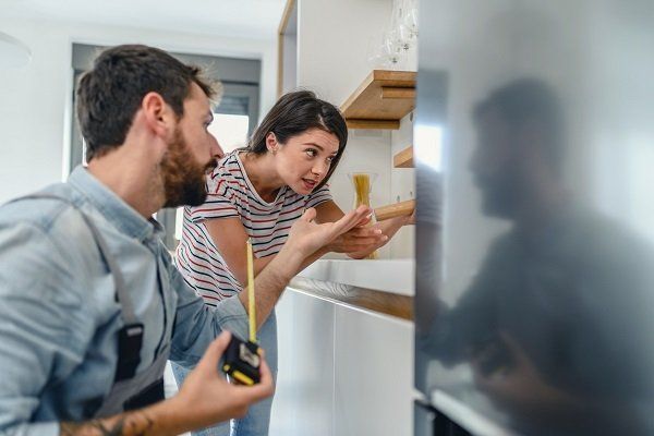 Un hombre y una mujer están midiendo un refrigerador en una cocina.