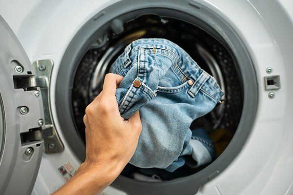 Una persona saca un par de jeans de una lavadora.