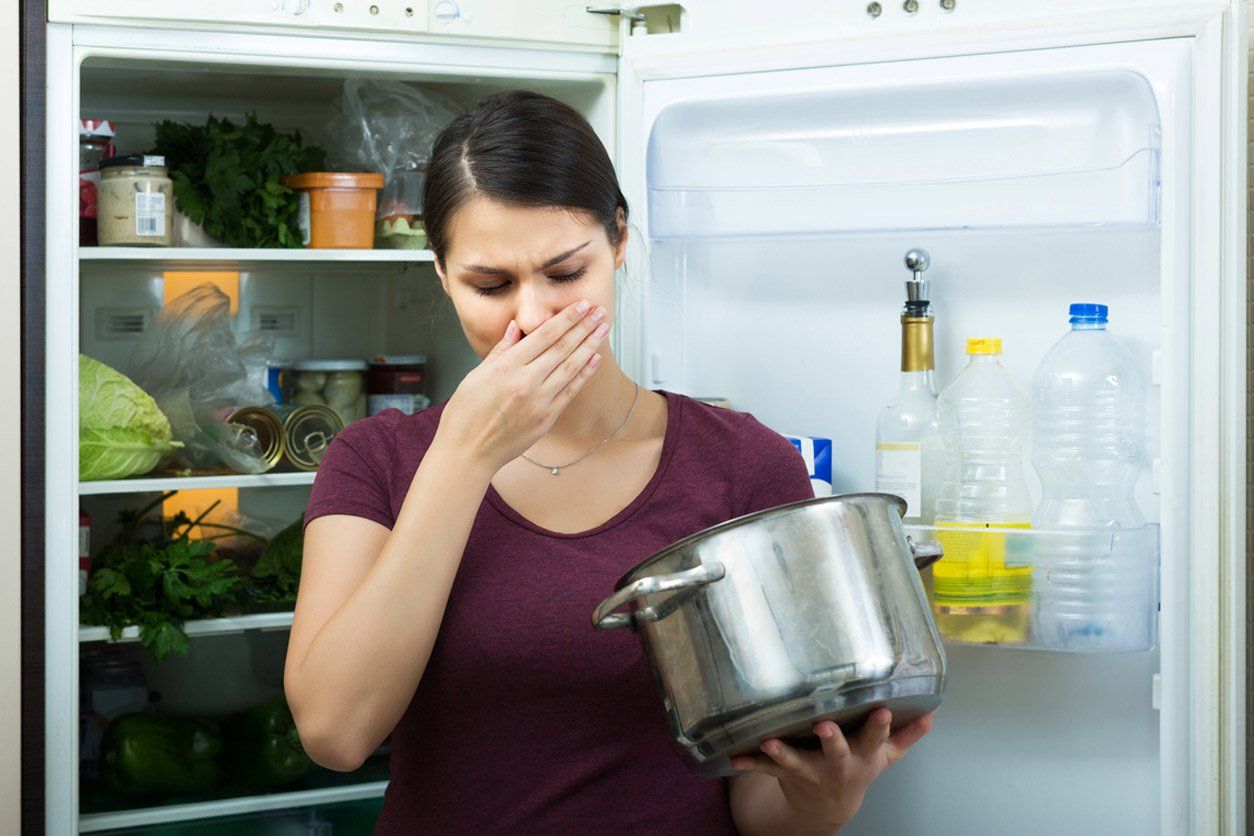 Una mujer sostiene una olla frente a un refrigerador abierto.