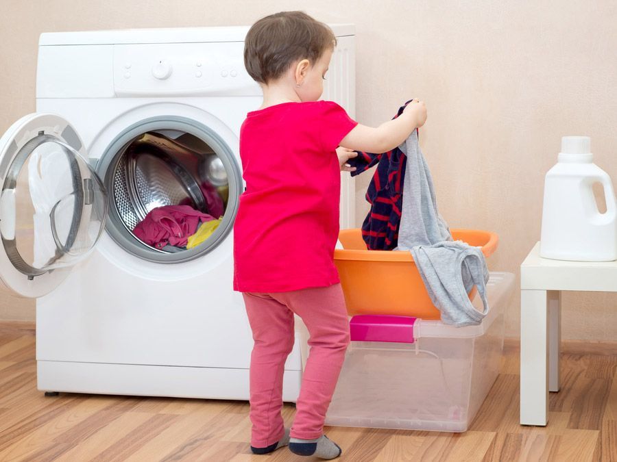 Un niño pequeño está poniendo ropa en una lavadora.