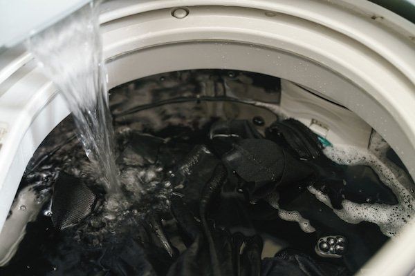 Una lavadora está llena de ropa negra y se vierte agua en ella.