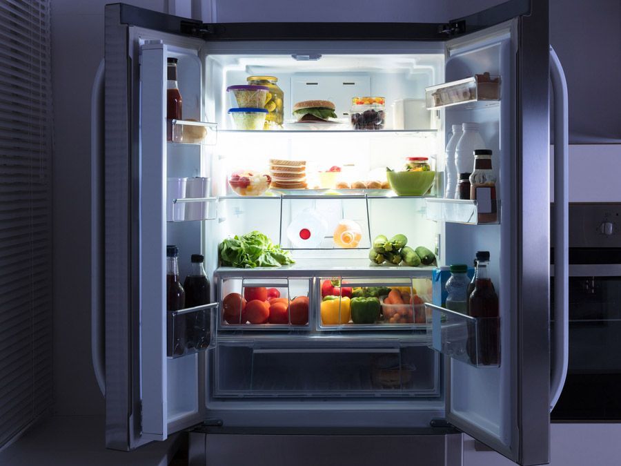 Un frigorífico abierto lleno de frutas y verduras por la noche.