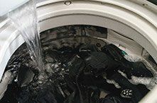 Una lavadora está llena de ropa negra y se vierte agua en ella.