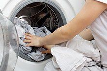 Una mujer está poniendo ropa en una lavadora.
