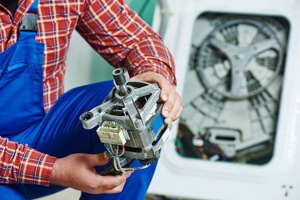 Un hombre sostiene un motor en sus manos frente a una lavadora.