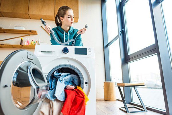 Una mujer está sentada encima de una lavadora sosteniendo un control remoto.