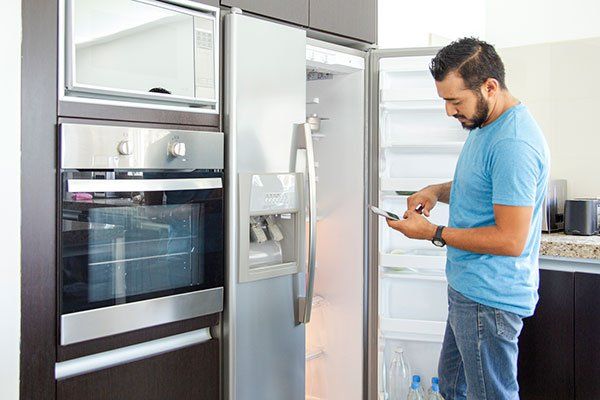 Un hombre está parado frente a un refrigerador mirando su teléfono.