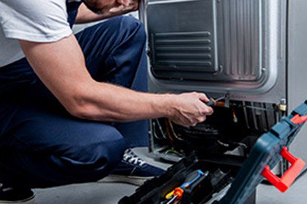 Un hombre está arrodillado en el suelo arreglando un refrigerador.