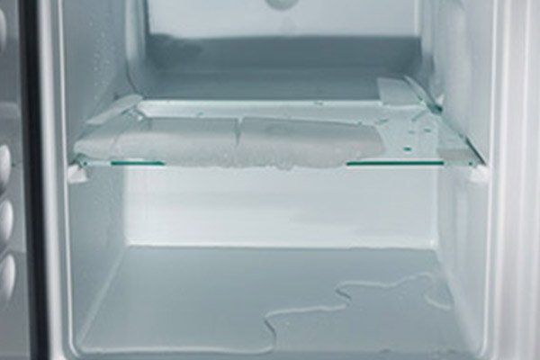 El interior de un frigorífico vacío con hielo en los estantes.
