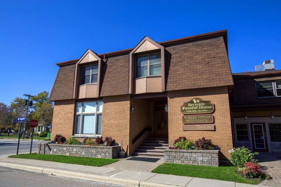 Brick two-story building with white columns, front porch, and trees along the sidewalk.