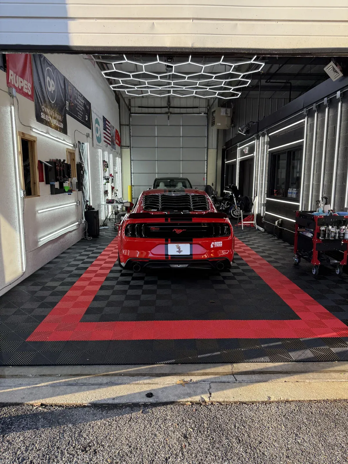 Red Mustang car inside a car detailing shop, surrounded by detailing tools and hexagon lights.