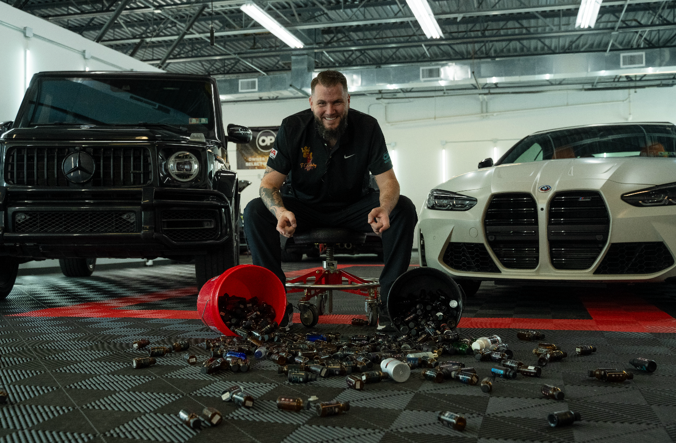 Orange Ford Mustang Shelby, black rims, parked next to a blue truck, in a garage with tiled floors.