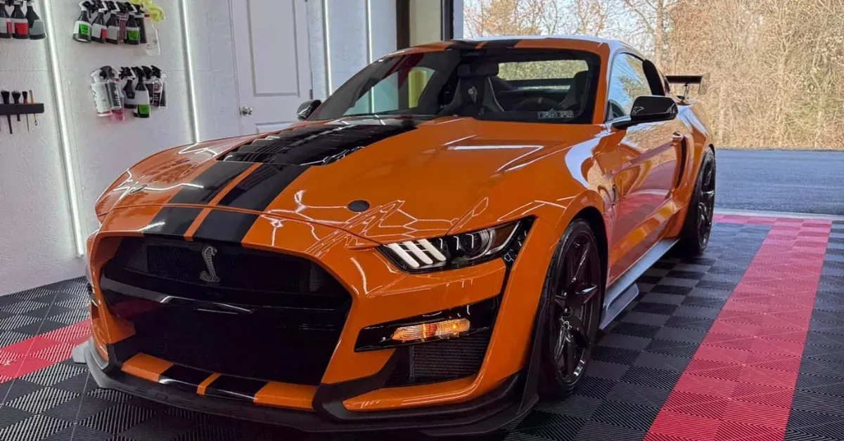 Orange Ford Mustang Shelby with black stripes in a garage.