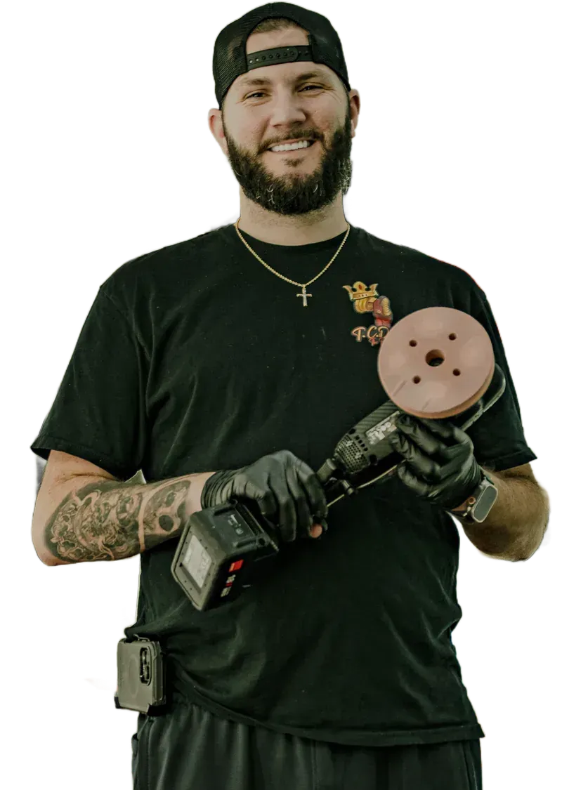 Man holding a polishing tool, wearing a black shirt, and a hat. He's smiling with a beard and gloves.