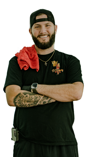 Man in black shirt with arms crossed, smiling, wearing a hat and watch, red towel on shoulder, outdoor.