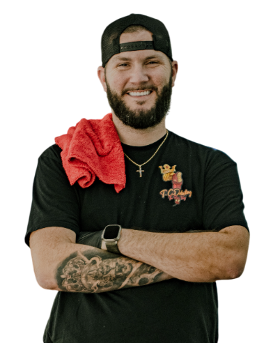 Man in black shirt and hat with crossed arms, red towel on shoulder, smiling.