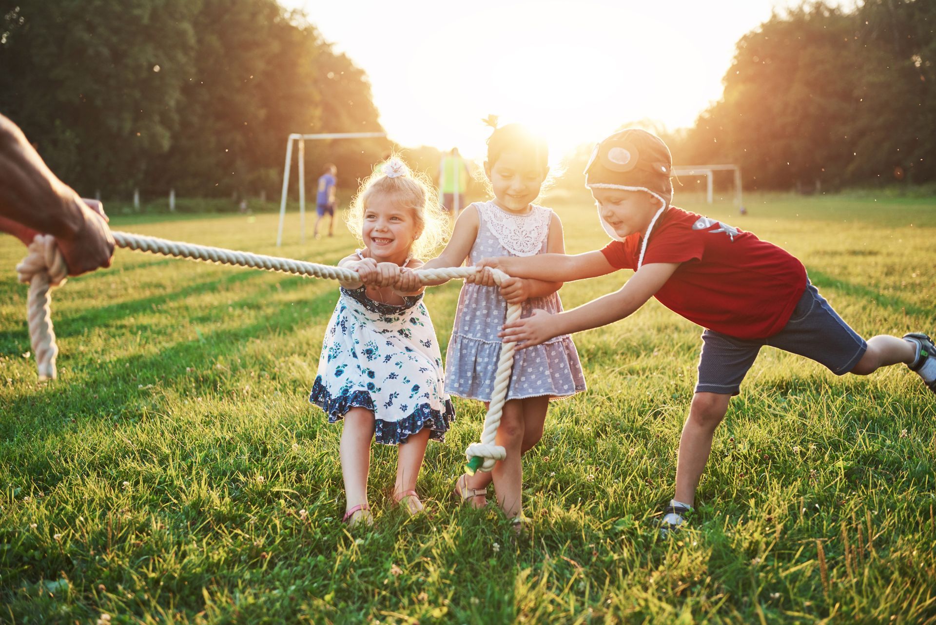 A boy and two girls are pulling a rope in a field.