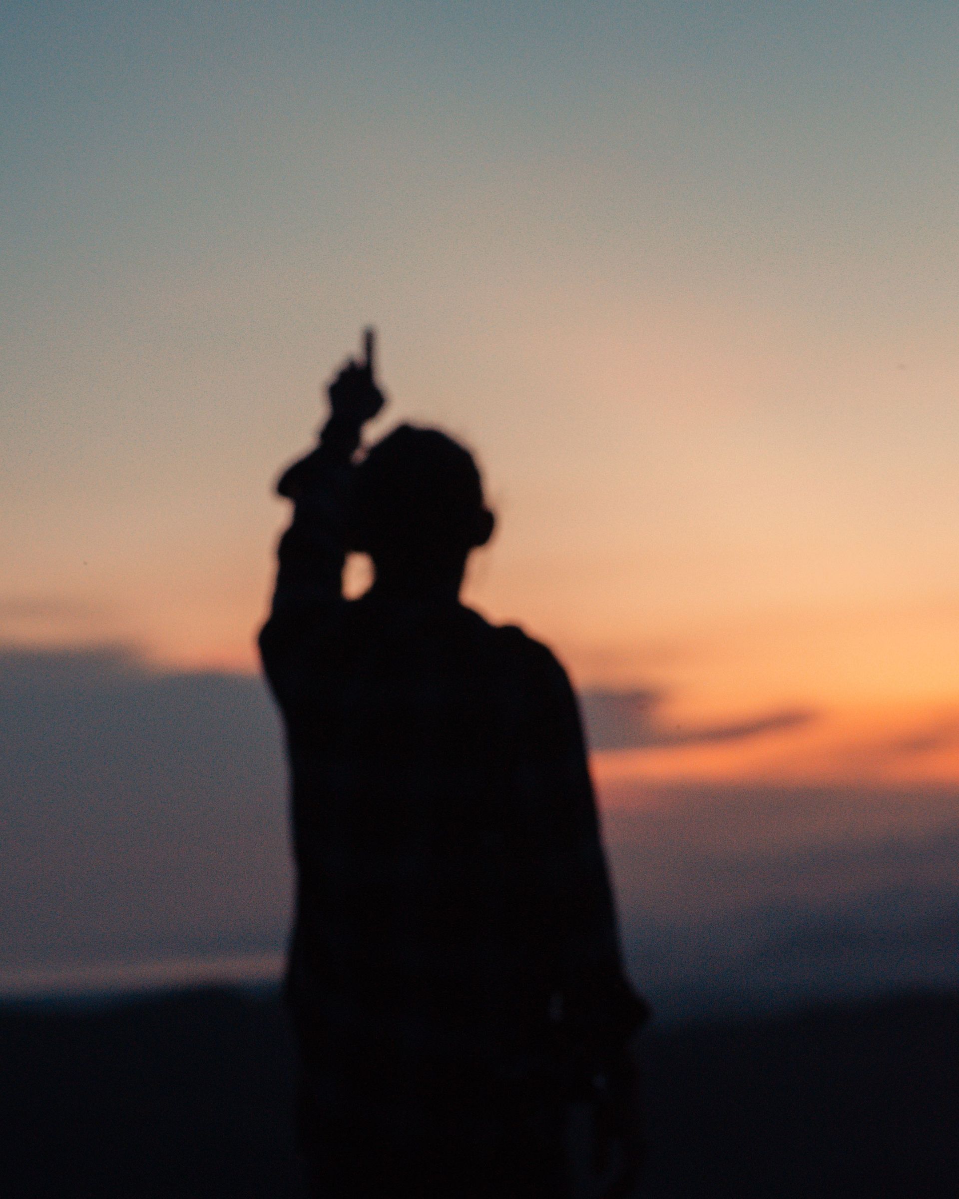 A person is standing in front of a sunset and pointing at the sky.
