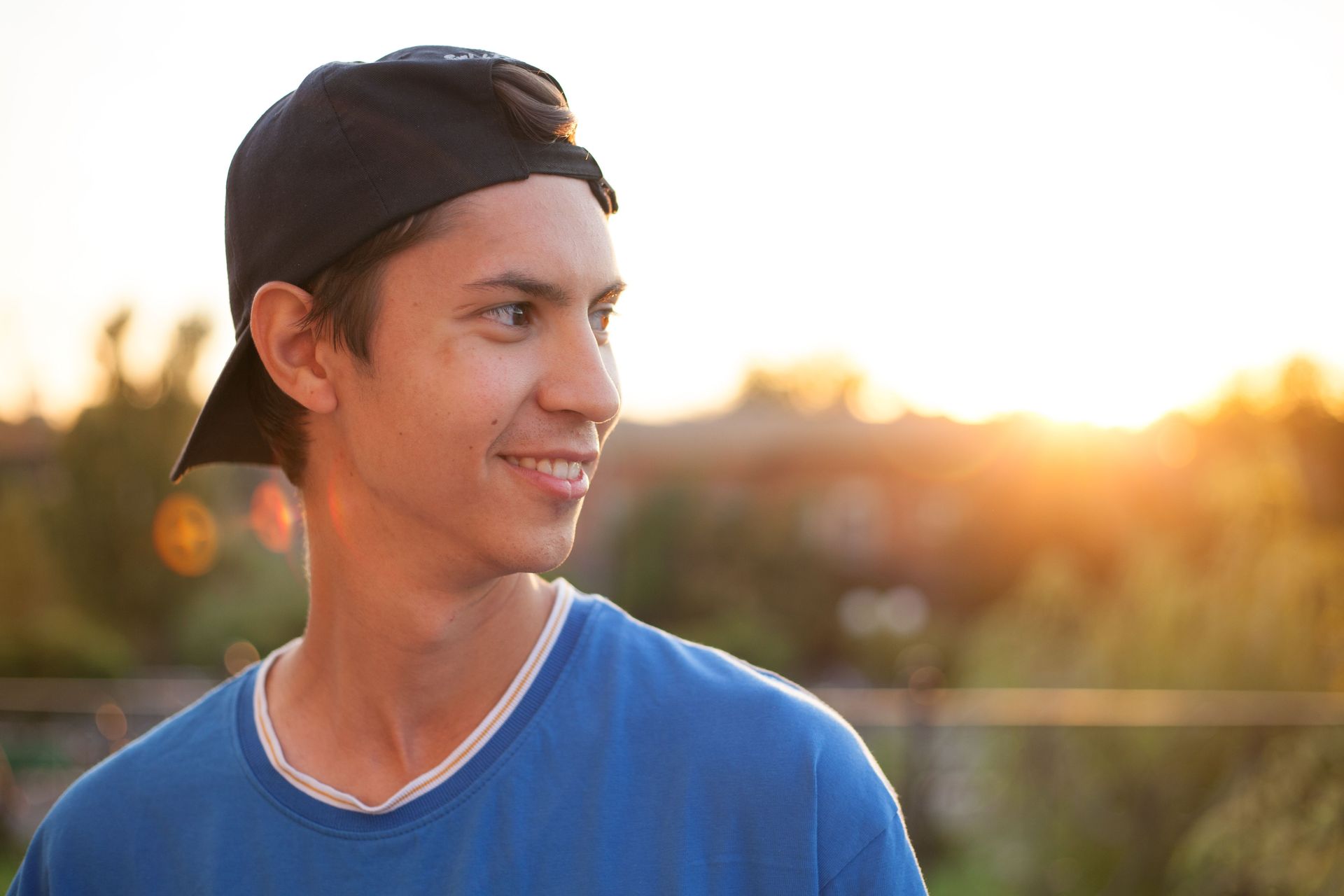 A male teenager is standing outside with a backwards baseball cap on.