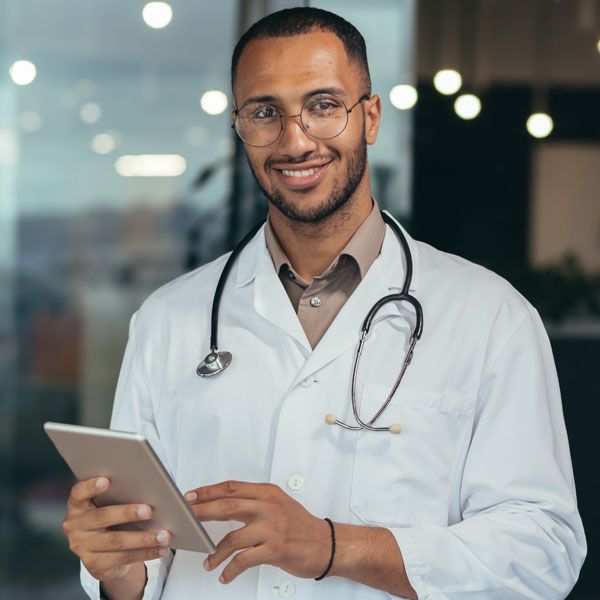 Smiling doctor in a white coat holding a tablet in a modern office