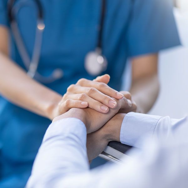 Healthcare worker placing hands on a patient’s hands in a supportive gesture